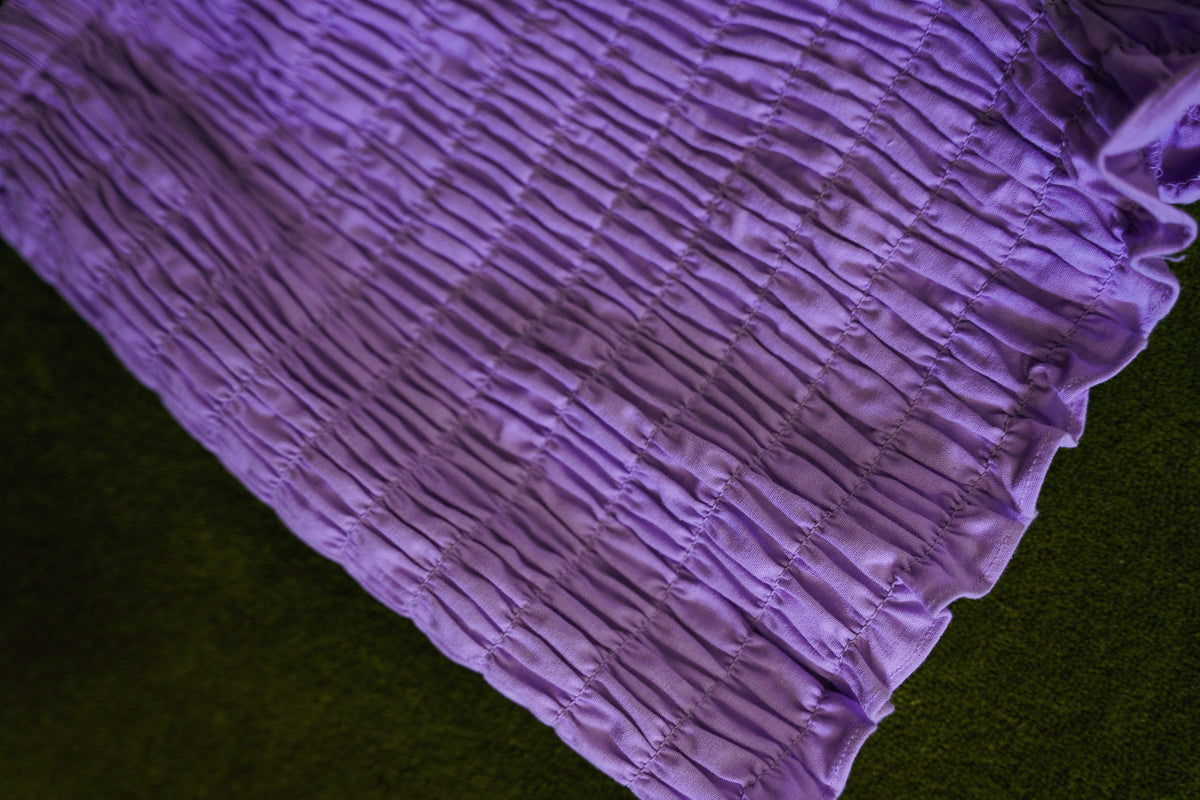 Close-up of purple cotton bloomers showing all-over elastic smocking and softly ruffled leg openings.