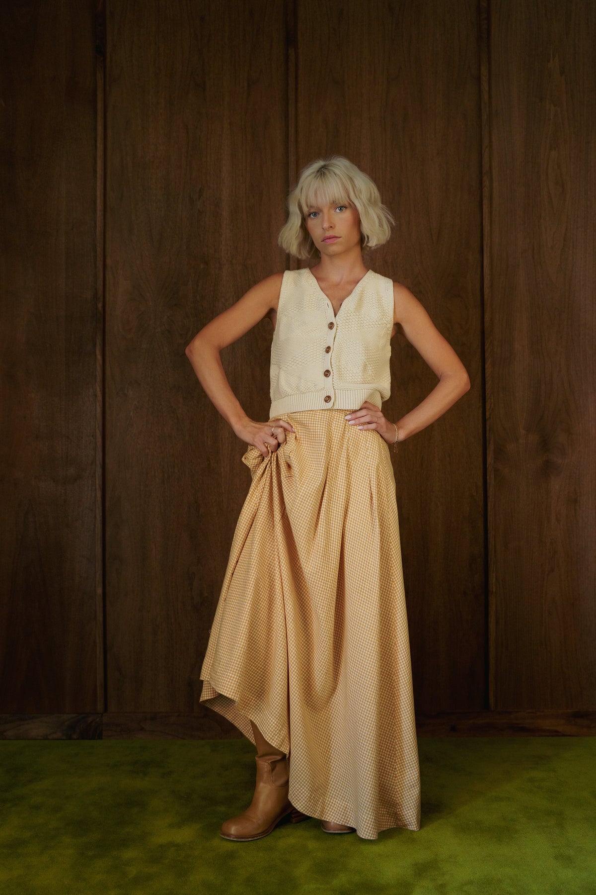 Rosemary Skirt in CandyCorn gingham styled with a cream vest and brown boots, with the hem lifted to show movement.